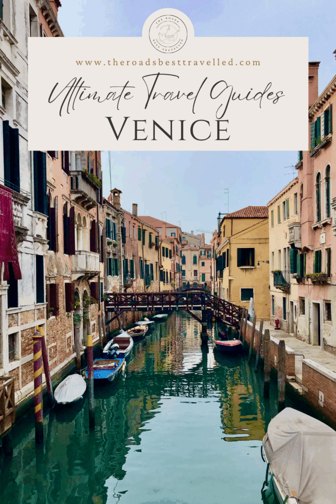 A quiet canal in Venice lined with colorful old buildings and moored boats, with a wooden pedestrian bridge in the distance under a clear sky. This serene view captures the charm of Venice’s backstreets—ideal for travellers looking for what to do in Venice in 1 day, including exploring lesser-known canals away from the crowds.