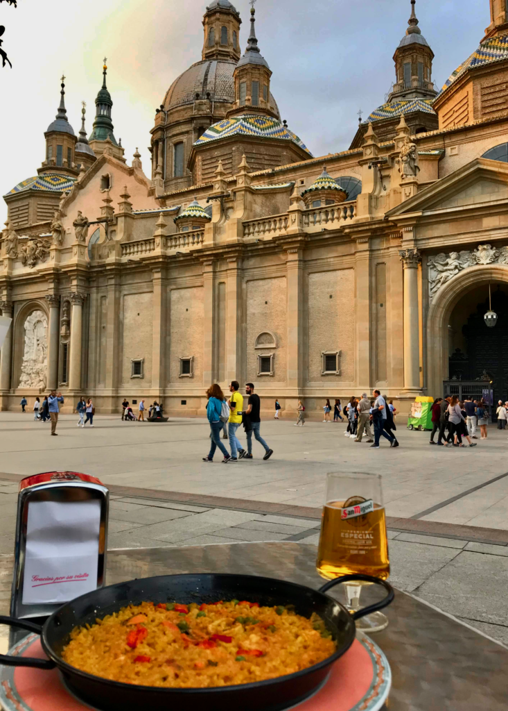 Paella dish on table in front of a cathdral. 