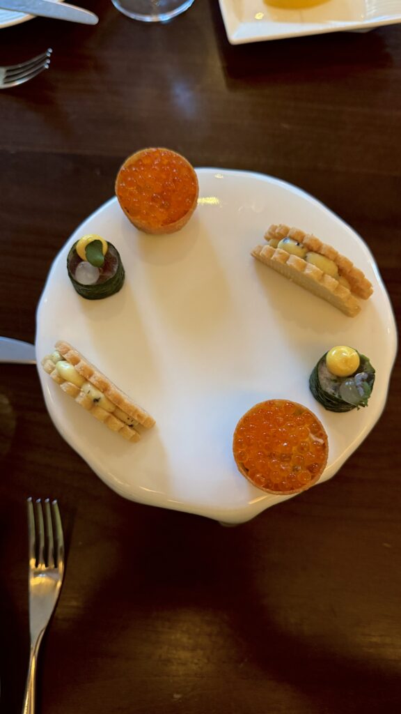 Artfully plated small bites at Four Seasons Toronto featuring delicate tartlets topped with bright orange roe and layered savory wafers arranged on a white plate. The refined presentation and elegant tasting course create a luxurious dining experience perfect for valentine’s day in Canada.