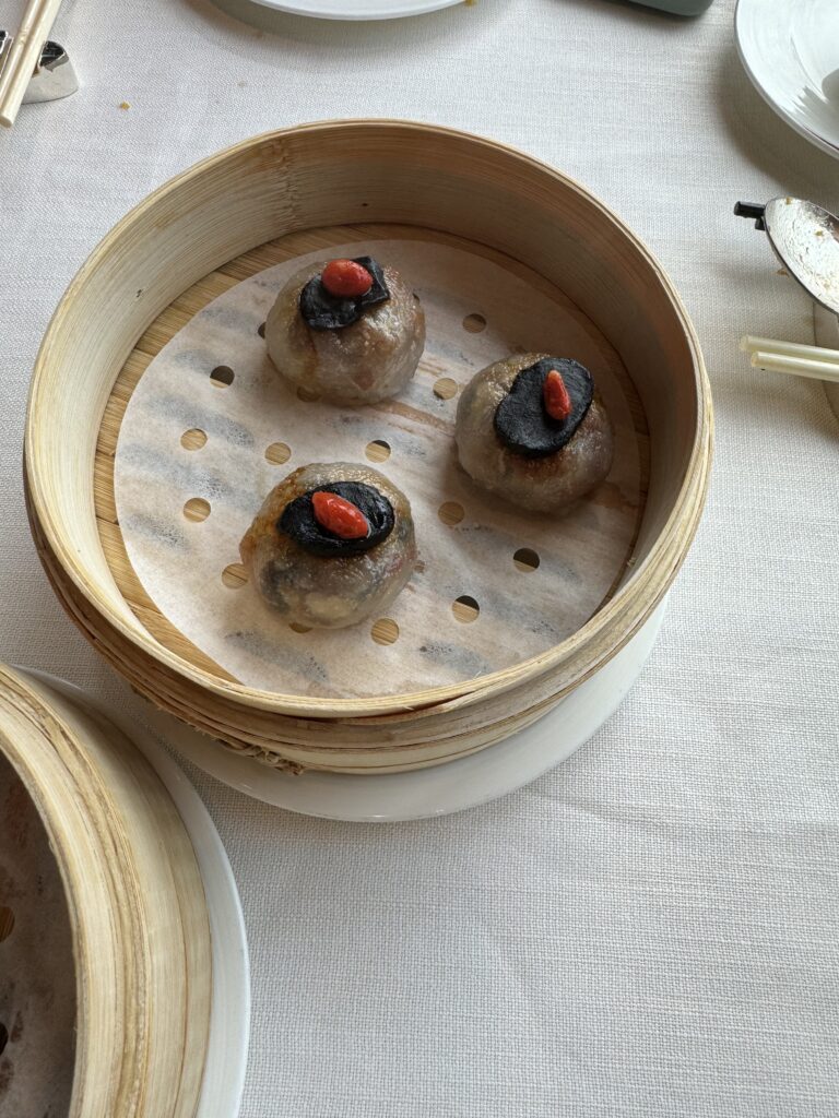 Bamboo steamer holding three glutinous truffle dumplings, each topped with a black truffle slice and a red goji berry, served at the Ritz-Carlton Hong Kong. A luxurious take on traditional Hong Kong food with modern elegance.