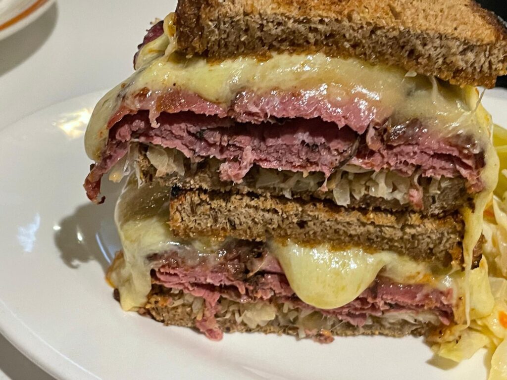 Close-up of a stacked pastrami Reuben sandwich on rye bread, loaded with melted Swiss cheese and sauerkraut. A bold and satisfying deli bite enjoyed during one day in Hong Kong.