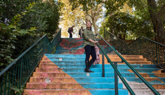 Woman standing on a painted stairway. The stairs are painted with pictures of flowers in orange and blue.