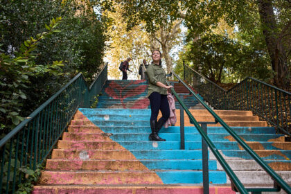 Woman standing on a painted stairway. The stairs are painted with pictures of flowers in orange and blue.