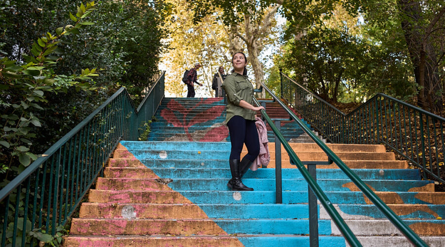 Woman standing on a painted stairway. The stairs are painted with pictures of flowers in orange and blue.