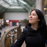 woman wearing black coat inside the train station in paris, france. She is thinking how to pack a carry on for 3 weeks in europe.