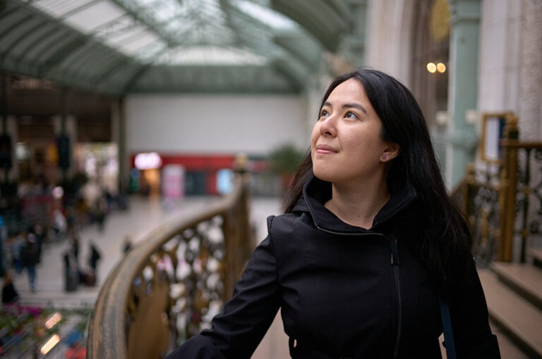 woman wearing black coat inside the train station in paris, france. She is thinking how to pack a carry on for 3 weeks in europe.