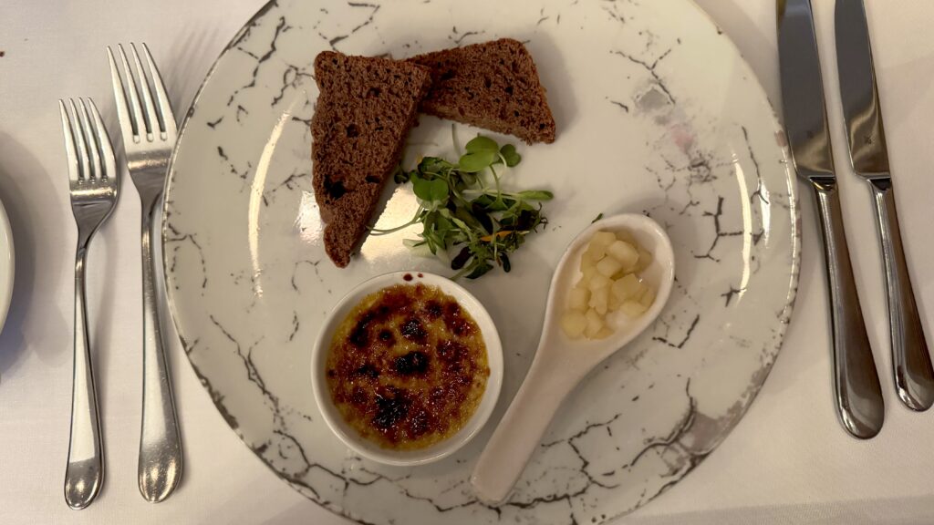 A beautifully plated multi-course meal at Bonaparte Restaurant in Montreal, starting with foie gras crème brûlée served with rye toast, diced pears, and microgreens, followed by a savoury phyllo pastry with rich demi-glace and a petite salad, and finishing with seared venison medallions in a berry sauce, grilled zucchini, asparagus, and baby potatoes. This elegant French fine dining experience is a highlight of any long weekend in Montreal.