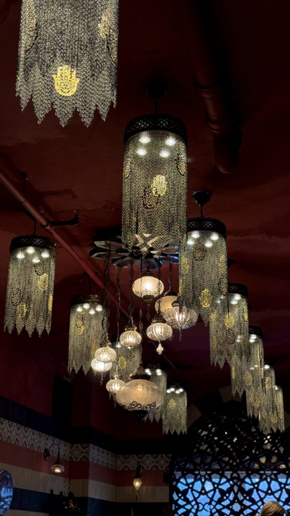An ornate ceiling display at Damas, a Syrian restaurant in Montreal, featuring glowing Moroccan-style lanterns and intricate metal chandeliers with golden hamsa designs, creating a warm, atmospheric setting ideal for a long weekend in Montreal. The rich red walls and patterned decor add to the luxurious Middle Eastern ambiance.