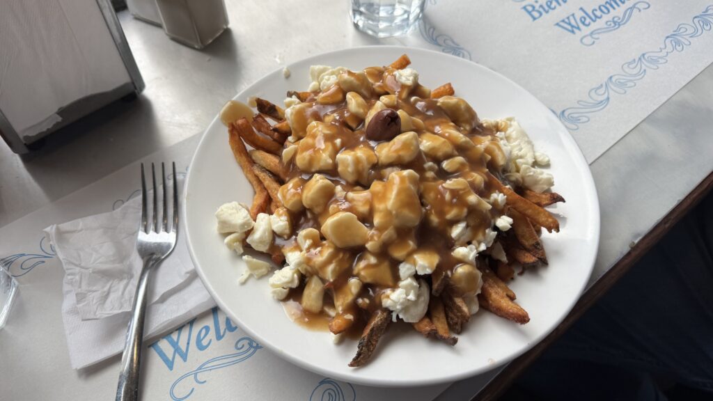 Alt text: A classic plate of poutine topped with rich brown gravy, fresh cheese curds, and a single olive sits on a white plate at a diner table. This iconic Québécois dish is a must-try at many beloved places to eat in Montreal.