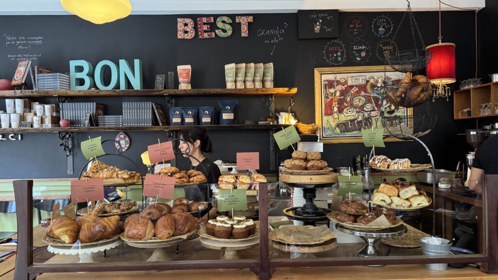 A cozy Montreal café with a colourful “BON” and “BEST” display on the wall behind a pastry counter filled with croissants, brioches, muffins, scones, and other fresh baked goods, offering a perfect morning stop during a long weekend in Montreal.