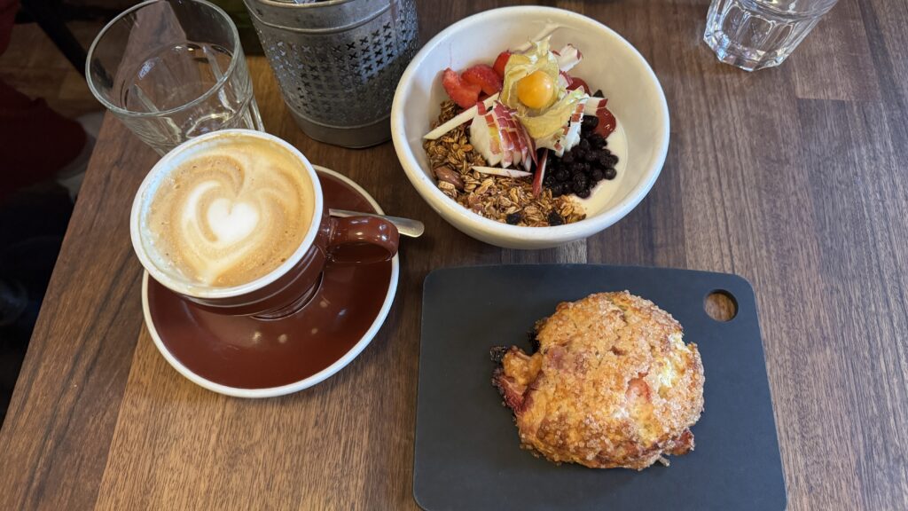 A cup of coffee, yogurt bowl, and scone on a wooden table. The perfect breakfast during your long weekend in montreal.