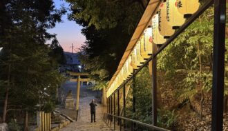 Stone steps descend toward a torii gate at Hachi Shrine in Kyoto as rows of glowing paper lanterns illuminate the path at dusk. The peaceful shrine setting showcases a lesser known stop that can be included in a Kyoto 1 day itinerary for travelers exploring the city’s historic neighborhoods after sunset.