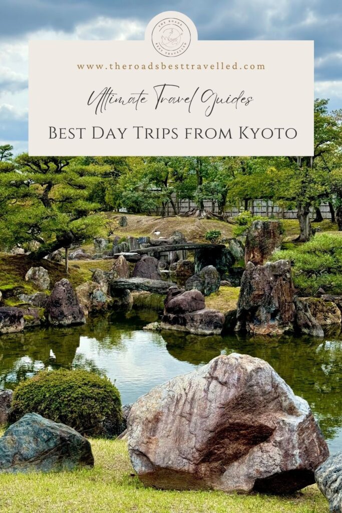 Image: uploaded image
Alt text: Japanese garden with large stone formations, a reflective pond, and carefully pruned trees beneath cloudy skies. Text on the image reads “www.theroadsbesttravelled.com” “Ultimate Travel Guides” and “Best Day Trips From Kyoto” highlighting scenic destinations popular with first time travellers visiting Kyoto.