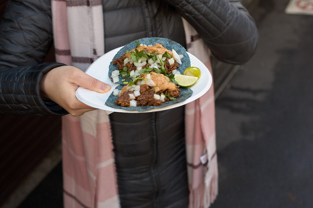 Traveler holds a plate of street style tacos topped with chopped onions, cilantro, and lime after ordering from a small food stand in Kyoto. Sampling unique local and international flavors along the way adds a memorable food stop to a Kyoto 1 day itinerary.