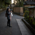 Traveler standing on a quiet residential street in Kyoto at dusk while checking directions on a smartphone. Walking through Kyoto’s historic neighborhoods is one of the best ways of getting around Kyoto, allowing visitors to discover hidden temples, local streets, and cultural landmarks between major attractions.