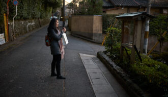 Traveler standing on a quiet residential street in Kyoto at dusk while checking directions on a smartphone. Walking through Kyoto’s historic neighborhoods is one of the best ways of getting around Kyoto, allowing visitors to discover hidden temples, local streets, and cultural landmarks between major attractions.