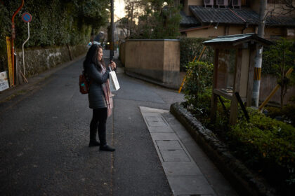 Traveler standing on a quiet residential street in Kyoto at dusk while checking directions on a smartphone. Walking through Kyoto’s historic neighborhoods is one of the best ways of getting around Kyoto, allowing visitors to discover hidden temples, local streets, and cultural landmarks between major attractions.