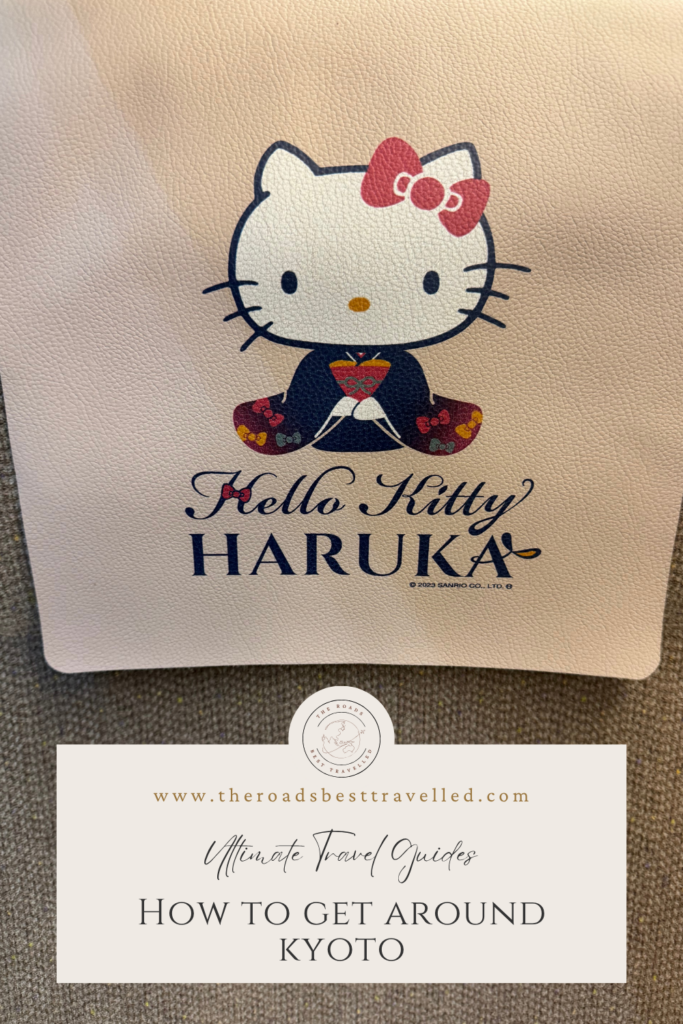 Hello Kitty HARUKA train branding featuring Hello Kitty dressed in a traditional kimono with a red bow on a cream colored background. Text on the image reads “Hello Kitty HARUKA” “www.theroadsbesttravelled.com” “Ultimate Travel Guides” and “How to Get Around Kyoto” highlighting one of the convenient train options travellers can use when getting around Kyoto and the surrounding region.